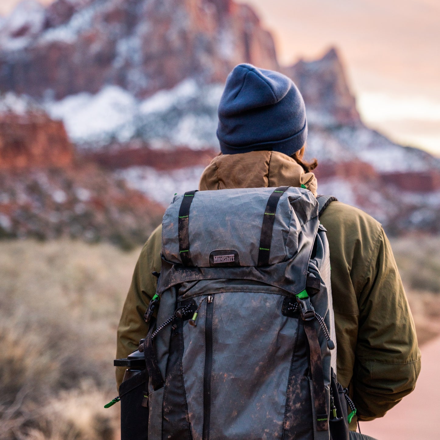 A man wearing a backpack, and a out of focus view of a mountain in the distance 