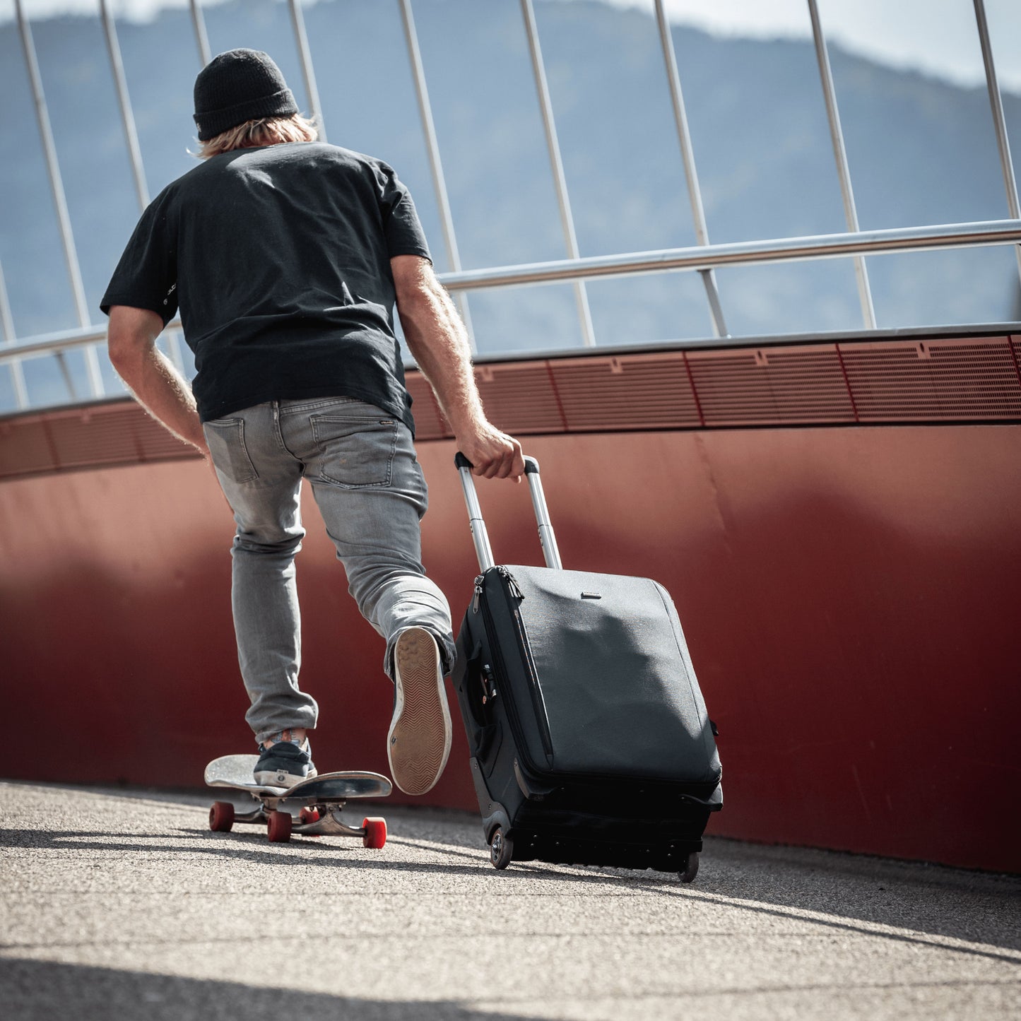 A person riding a skateboard, while rolling a suitcase behind him